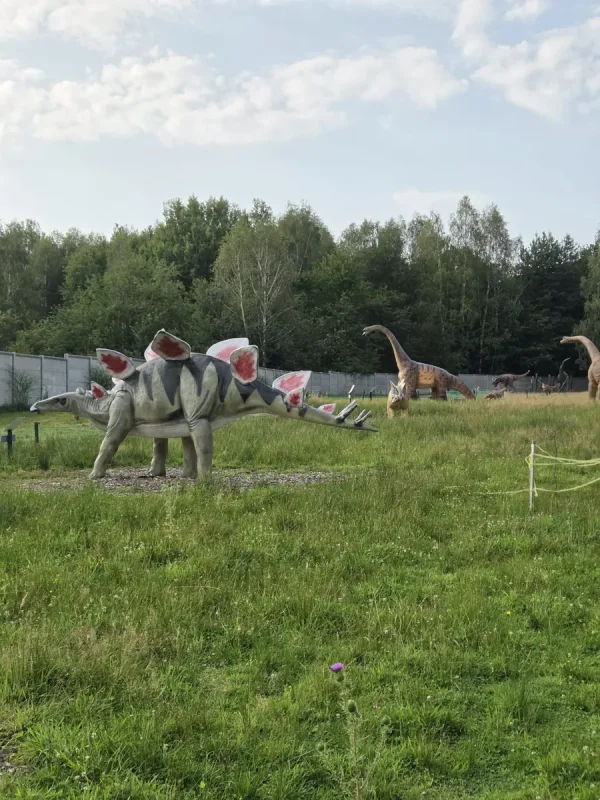 Figura stegozaura na łące, w tle brachiozaur i inne figury dinozaurów
