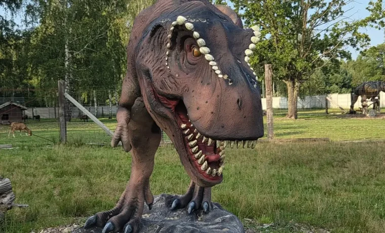 Figura T-Rexa z szeroko otwartą paszczą na skalnym cokole w parku dinozaurów Mini Zoo Dino