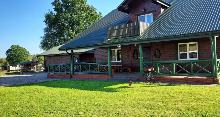 Drewniany domek noclegowy z werandą, trawnik w słońcu