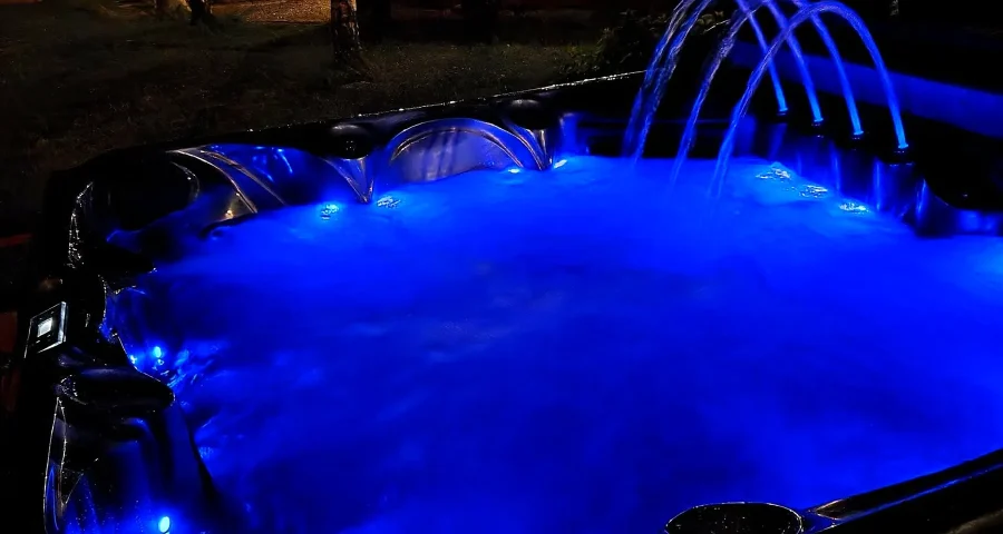 Jacuzzi na świeżym powietrzu nocą, podświetlone na niebiesko, z fontannami wody
