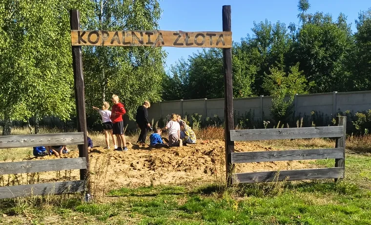 Dzieci kopią w piasku pod drewnianą bramą z napisem Kopalnia złota
