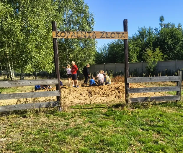 Uczniowie szukają skarbów w piasku pod bramą z napisem Kopalnia złota