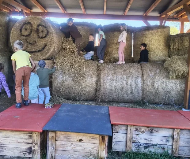 Przedszkolaki wspinają się po belach słomy pod drewnianą wiatą