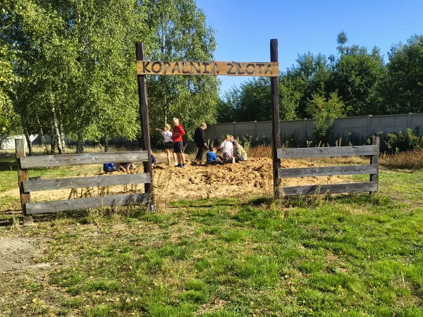 Dzieci kopią w piasku za bramą z napisem Kopalnia złota