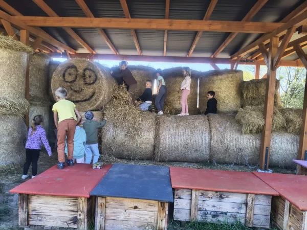 Dzieci wspinają się po belach słomy pod drewnianą wiatą