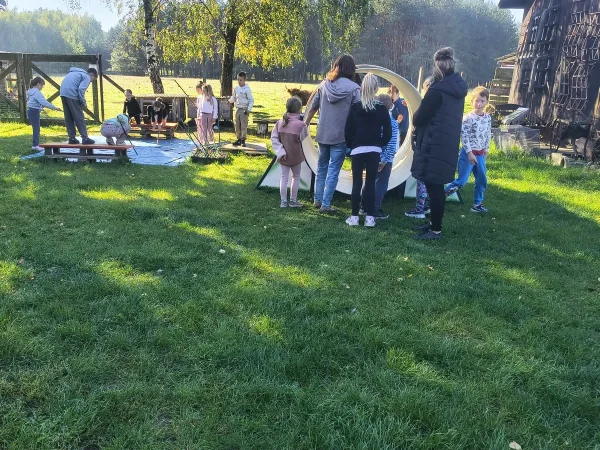 Dzieci z opiekunami przy stacjach zabaw na trawie, w tle krowy szkockie